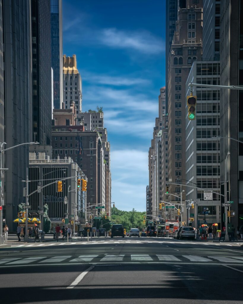 Wide city street lined with tall buildings under a blue sky — exploring US cities on a budget