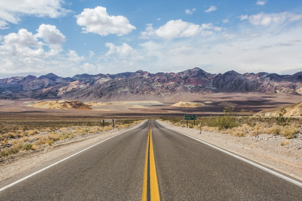 An open American highway stretching toward the horizon, representing budget road trip travel across the USA