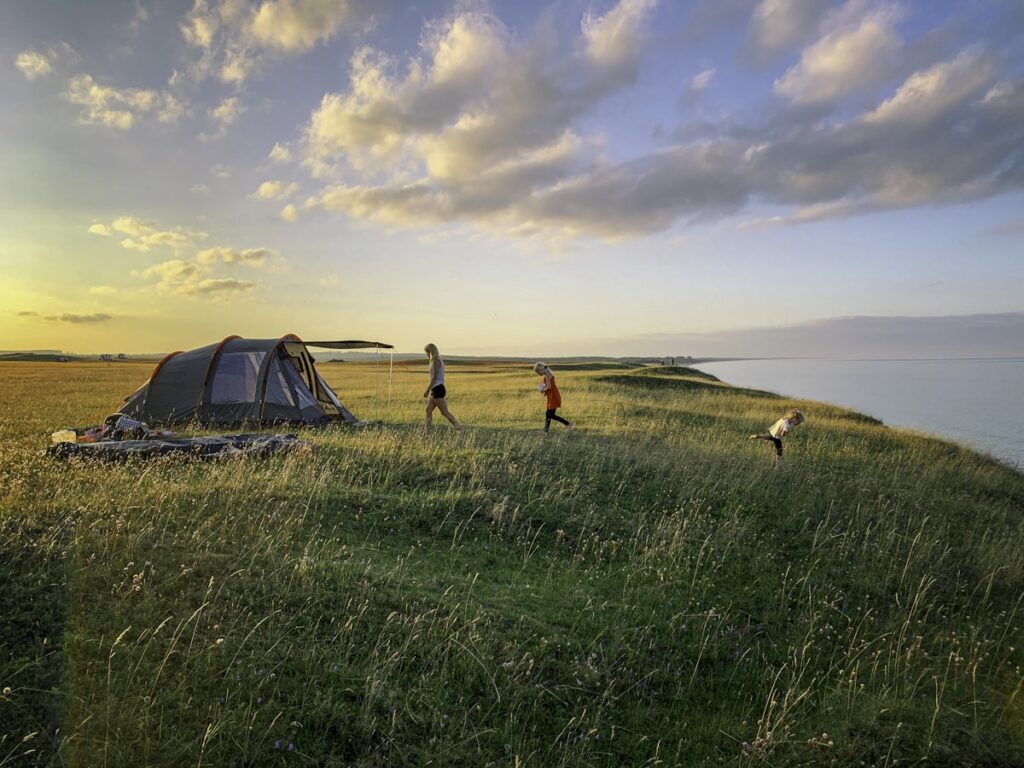 budget summer camping tips — toddler by family tent at golden hour